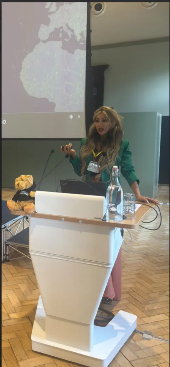 Zara speaking at a podium in front of a projected map